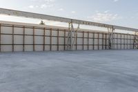 an empty lot with white concrete flooring and wall on the corner of it, under a metal structure