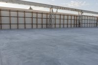 an empty lot with white concrete flooring and wall on the corner of it, under a metal structure