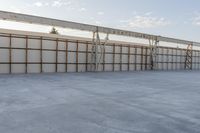 an empty lot with white concrete flooring and wall on the corner of it, under a metal structure