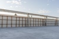 an empty lot with white concrete flooring and wall on the corner of it, under a metal structure