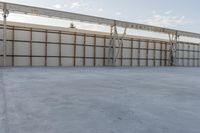 an empty lot with white concrete flooring and wall on the corner of it, under a metal structure