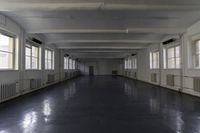 this is a long corridor in a building with many windows on the sides and light colored floors