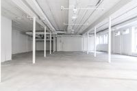 white warehouse space with concrete floors and large windows and beams that lead to a room
