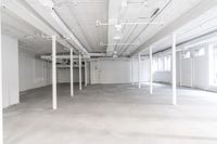white warehouse space with concrete floors and large windows and beams that lead to a room