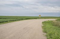 a dirt road with a sign on the side of it next to some tall grass