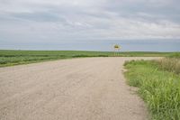 a dirt road with a sign on the side of it next to some tall grass