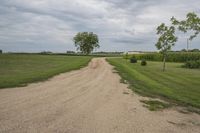 a dirt road with an asphalt path in front of a field, and a barn in the background
