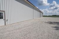 a driveway that has some gravel around it, and there is an airplane hangar behind the building