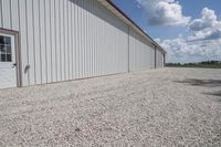 a driveway that has some gravel around it, and there is an airplane hangar behind the building