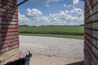 a barn on top of a gravel road next to grass and trees in front of a blue sky