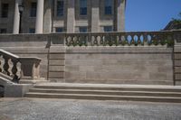 two concrete pillars line the wall on the outside side of a building with a large, stone balcony