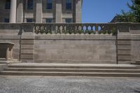 two concrete pillars line the wall on the outside side of a building with a large, stone balcony