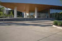 large building with curved roof over a walkway near trees and shrubs at the bottom of stairs