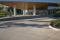 large building with curved roof over a walkway near trees and shrubs at the bottom of stairs