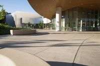 the large modern building is built out of concrete and features an entrance on one side, walkway on the other, and glass - covered in