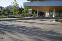 a large building that is outside in the sunlight on a sunny day and a little boy on a skate board is standing beside him