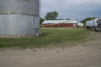 the semi truck is driving along the road near the large silo and barn buildings