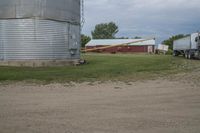 the semi truck is driving along the road near the large silo and barn buildings