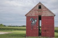 the old, weathered building has been painted with graffiti and is in a field with corn