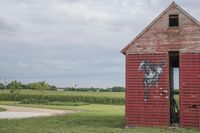 the old, weathered building has been painted with graffiti and is in a field with corn