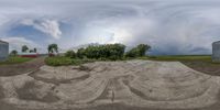 a circular shot of dirt in a field and houses with trees, clouds and a blue sky