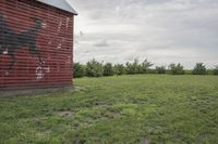 an old wooden barn with graffiti on it in the middle of grass area by trees