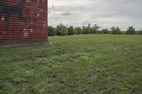 an old wooden barn with graffiti on it in the middle of grass area by trees