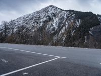 a mountain with a snow covered peak and trees in front of it on an empty road