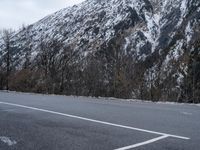 a mountain with a snow covered peak and trees in front of it on an empty road