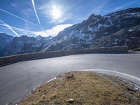 a mountain side with a curve road and sky in the background as viewed from below