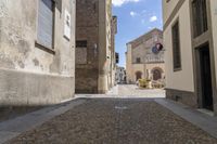 the corner of a narrow city street with a church behind it and a stone walkway in front of the buildings