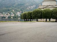 people walk through a park area with a hill in the background behind them and two benches on each side of the plaza