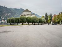 people walk through a park area with a hill in the background behind them and two benches on each side of the plaza