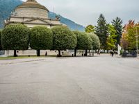 people walk through a park area with a hill in the background behind them and two benches on each side of the plaza