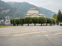 people walk through a park area with a hill in the background behind them and two benches on each side of the plaza