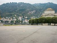 people walk through a park area with a hill in the background behind them and two benches on each side of the plaza