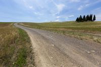 a dirt road that is surrounded by dry grass and hills at the side of a field