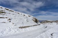 a snow - covered mountain is surrounded by a slope and two people are walking along the path