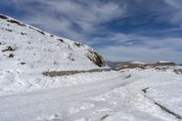 a snow - covered mountain is surrounded by a slope and two people are walking along the path