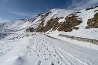 a mountain in snow with tracks left by the track in front of it and a road in the middle of the foreground