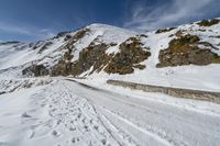 a mountain in snow with tracks left by the track in front of it and a road in the middle of the foreground