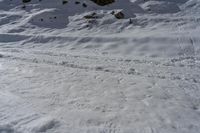 a person skiing down a snowy hill near rocks on a sunny day and another person walking