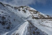 snow covered mountain top and a road winding through it, with a lone person walking on the other side