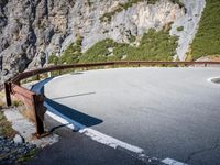 the long metal rail next to a steep cliff edge on a mountain road with rocks and green grass