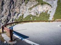 the long metal rail next to a steep cliff edge on a mountain road with rocks and green grass