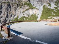 the long metal rail next to a steep cliff edge on a mountain road with rocks and green grass