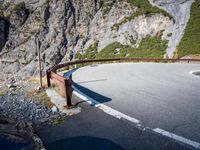 the long metal rail next to a steep cliff edge on a mountain road with rocks and green grass