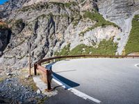 the long metal rail next to a steep cliff edge on a mountain road with rocks and green grass