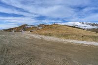 a dirt road leading down to a mountain covered with snow on the top of a hill