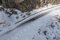 a road that is being worked by a man in skis in the snow near rocks and trees